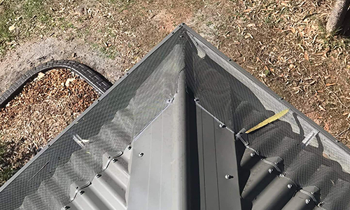 Gutter guard mesh fitted along the edges and corner of a dark metal roof